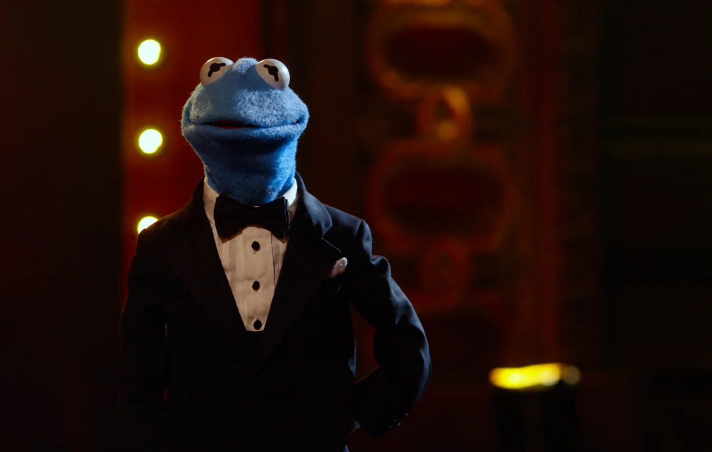 Froggin’s blue frog in a black tuxedo in a cinematic lounge